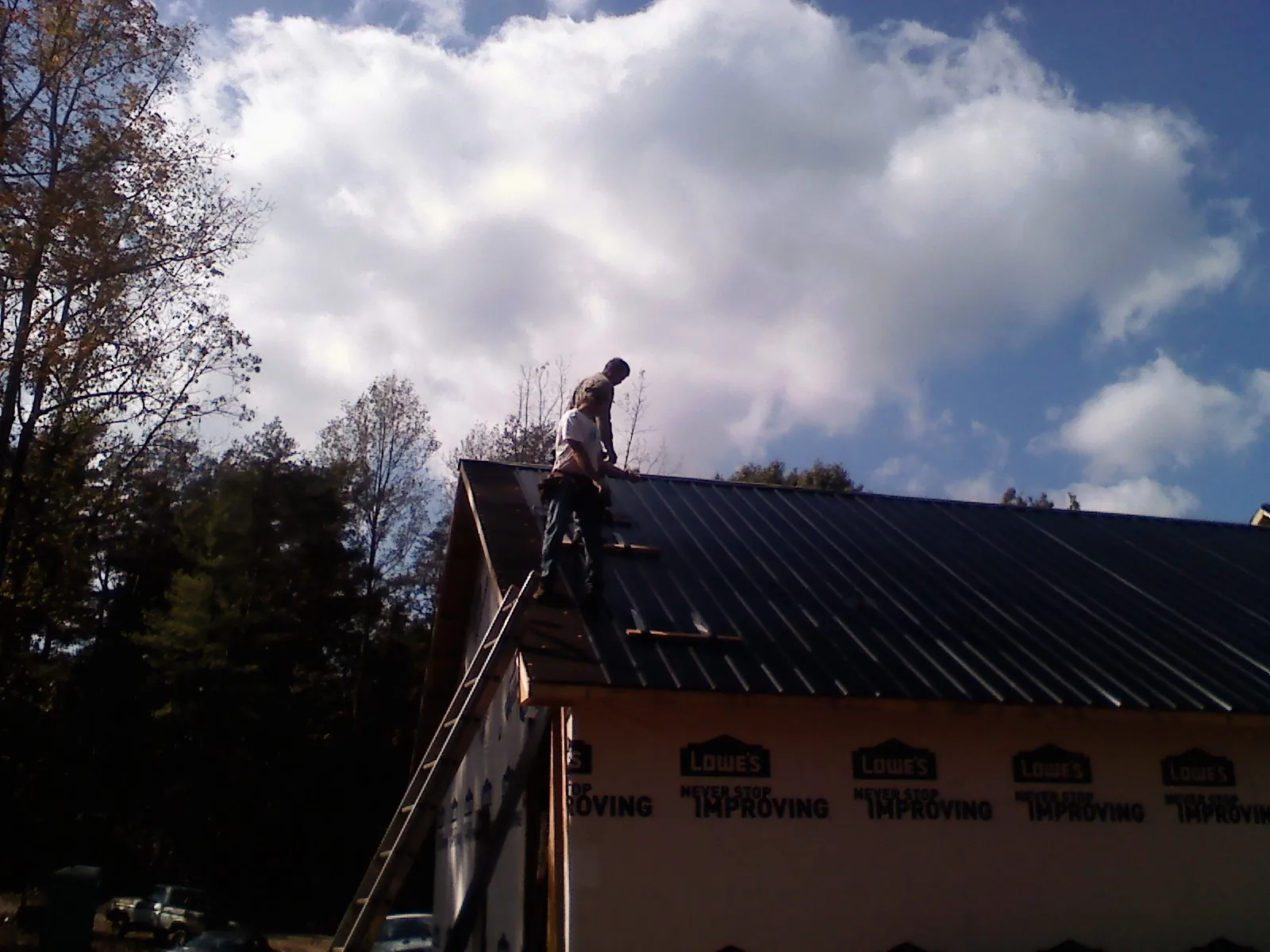 Roofer fastening dark metal panels high against a cloudy sky, from a Roof Inspection job in El Mirage