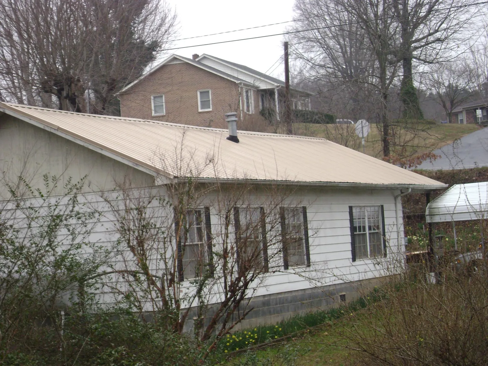 Tan metal roof on a white sided house set into a hillside — Commercial Roofing by Roofing Brothers in El Mirage